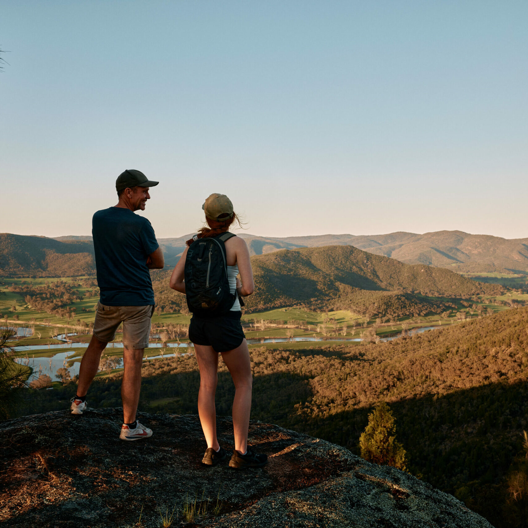 Two trekkers stand together on a lookout, taking in a sweeping, tranquil landscape along The Great River Road, embodying a peaceful escape into nature.