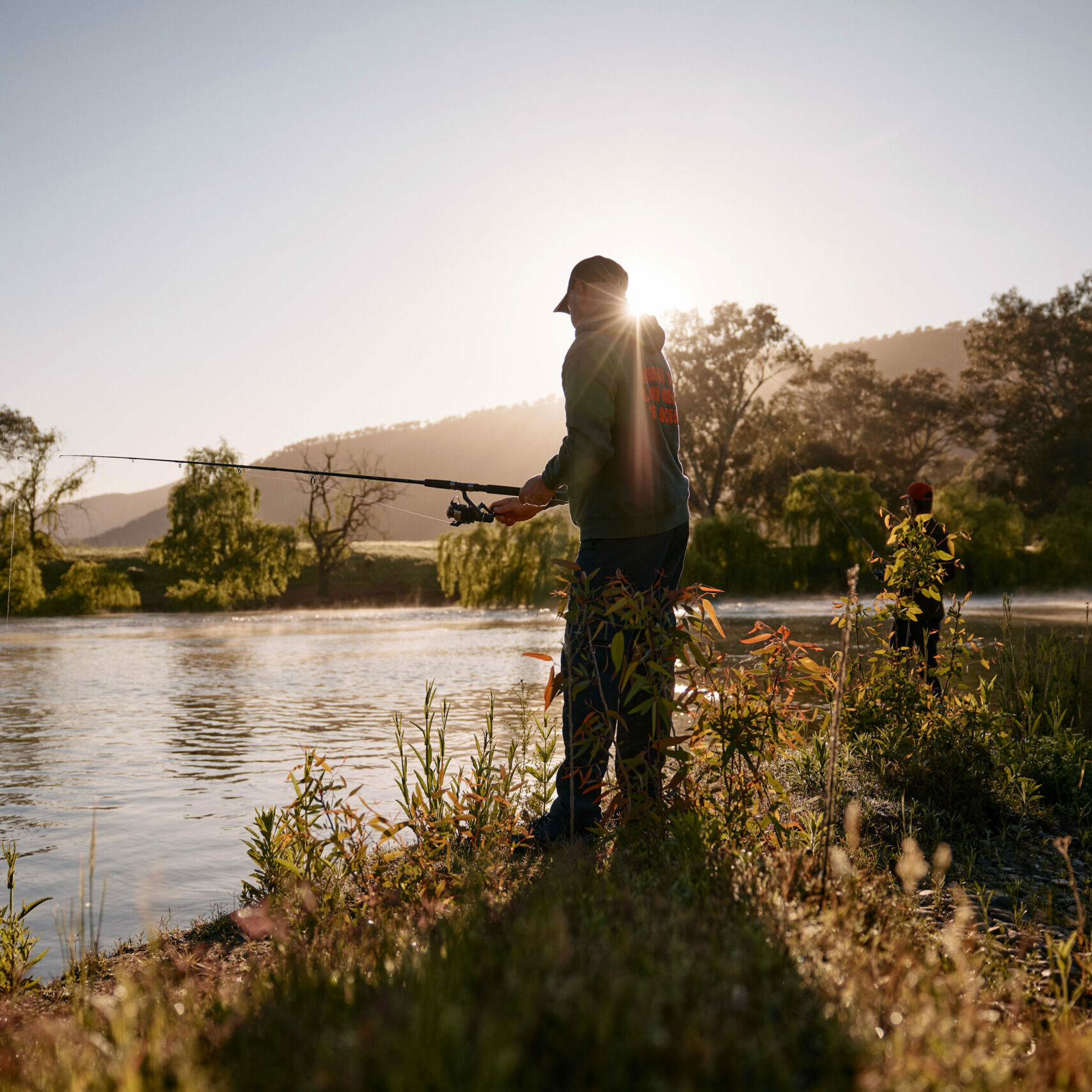 Man fishing by the river along the Upper Murray, set against a backdrop of scenic river views that highlight the abundant fishing spots of the Great River Road region.