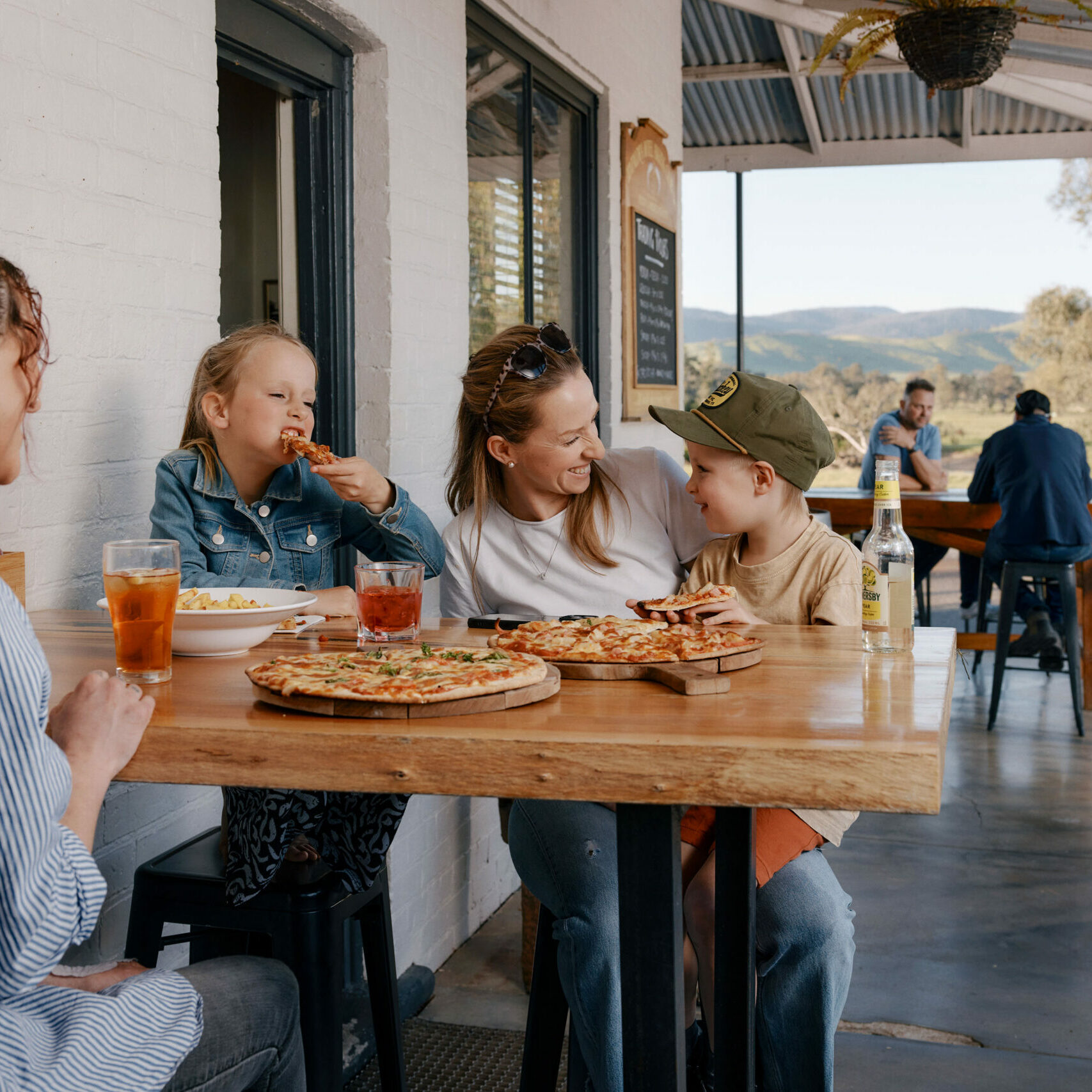 Family enjoying a meal and drinks at a country pub along the Murray River, capturing the warm hospitality and inviting pit stops of the Great River Road.