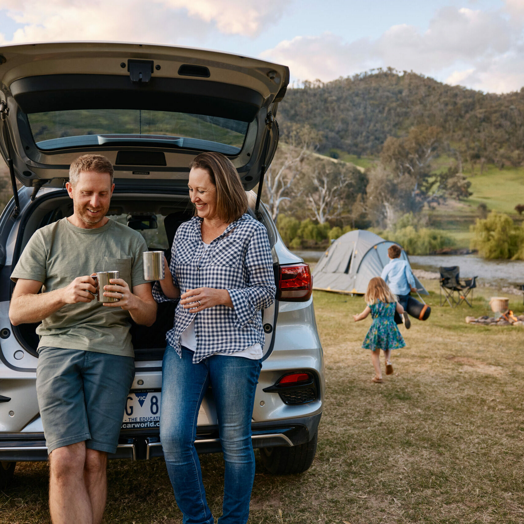 A couple enjoying a hot beverage at a caravan park while their kids play in the background, capturing the relaxed, family-friendly vibe of the scenic campgrounds along the route.